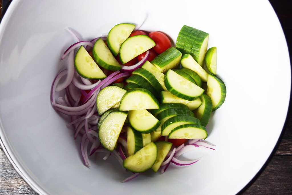 Cucumber salad vegetables in a white mixing bowl.