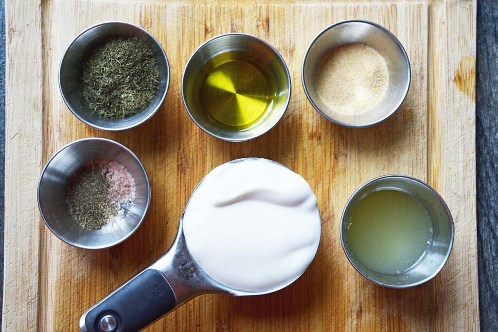 Dressing ingredients for cucumber salad sitting in individual cups on a wood cutting board.