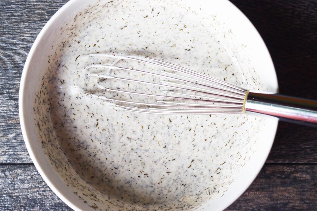 Cucumber salad dressing mixed together in a mixing bowl with a whisk.