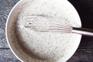 Cucumber salad dressing mixed together in a mixing bowl with a whisk.