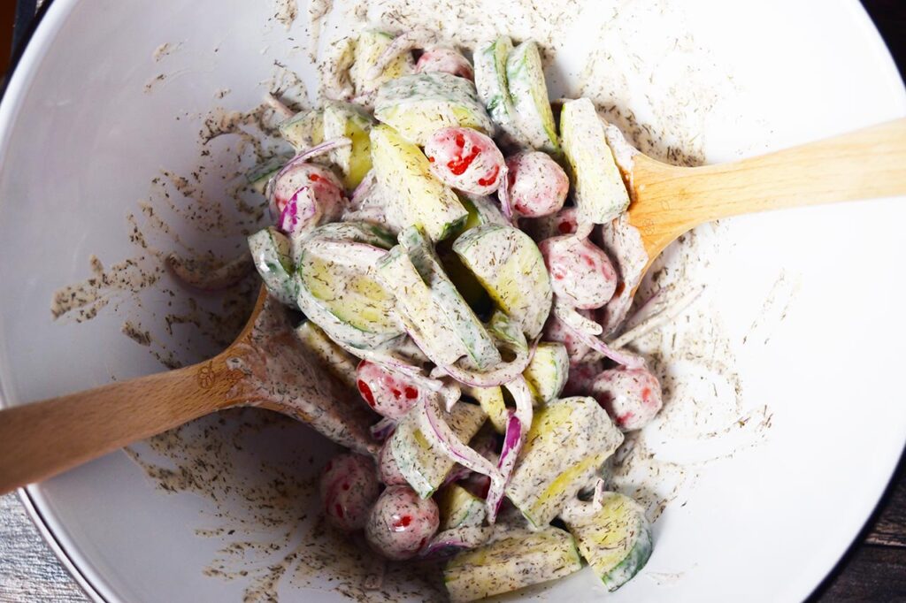 Cucumber salad mixed with dressing in a mixing bowl.