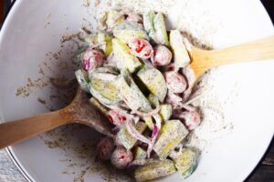 Cucumber salad mixed with dressing in a mixing bowl.