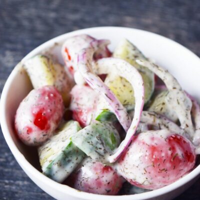 Angled front view of a white bowl full of cucumber salad.