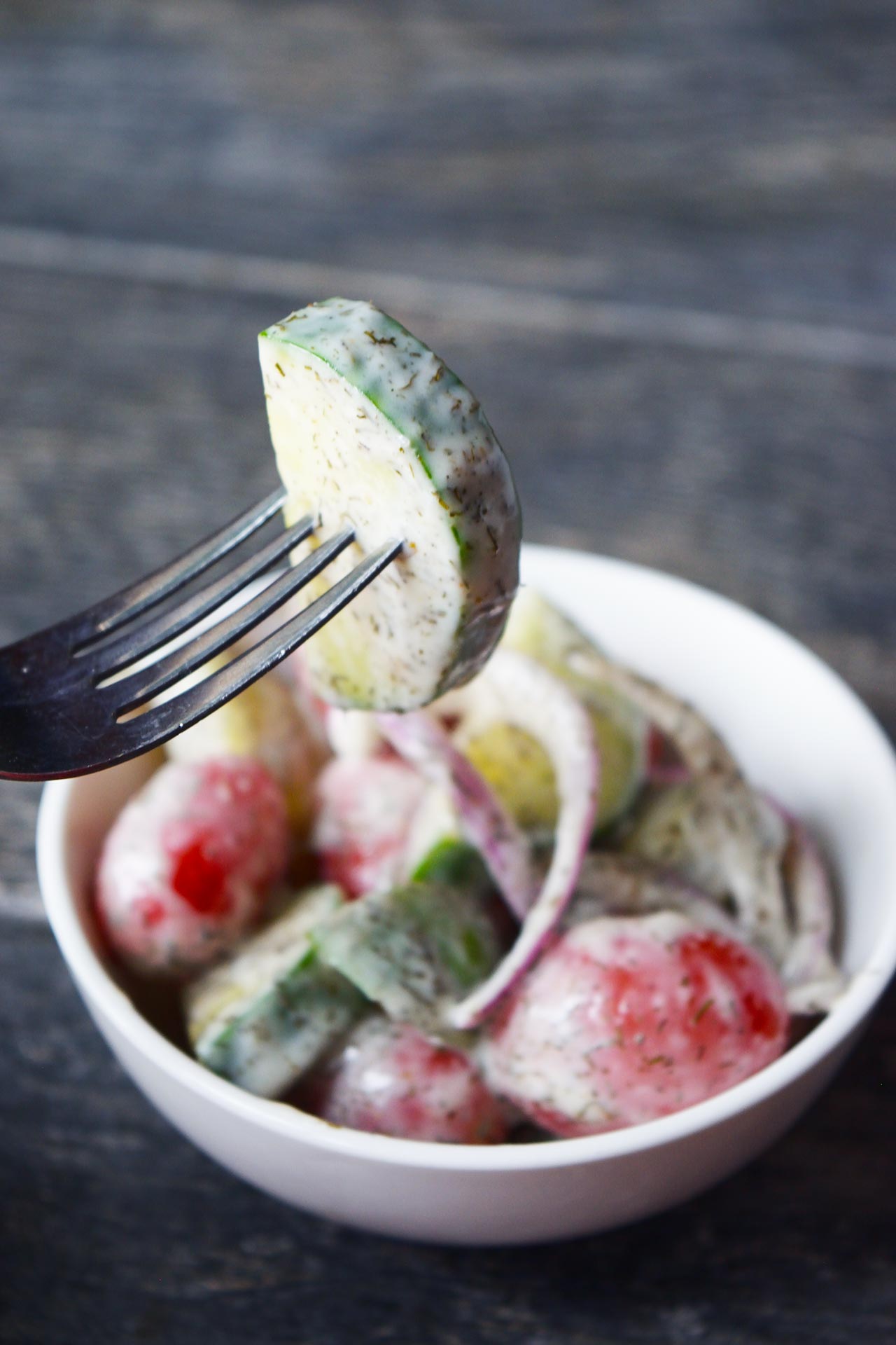 Side view of a fork lifting a piece of cucumber out of a white bowl filled with cucumber salad.