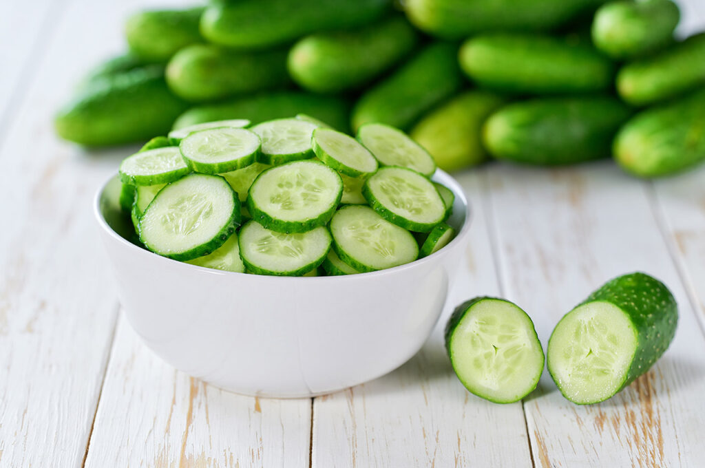 Organic cucumbers slices in a ceramic bowl on a light table, selective focus.