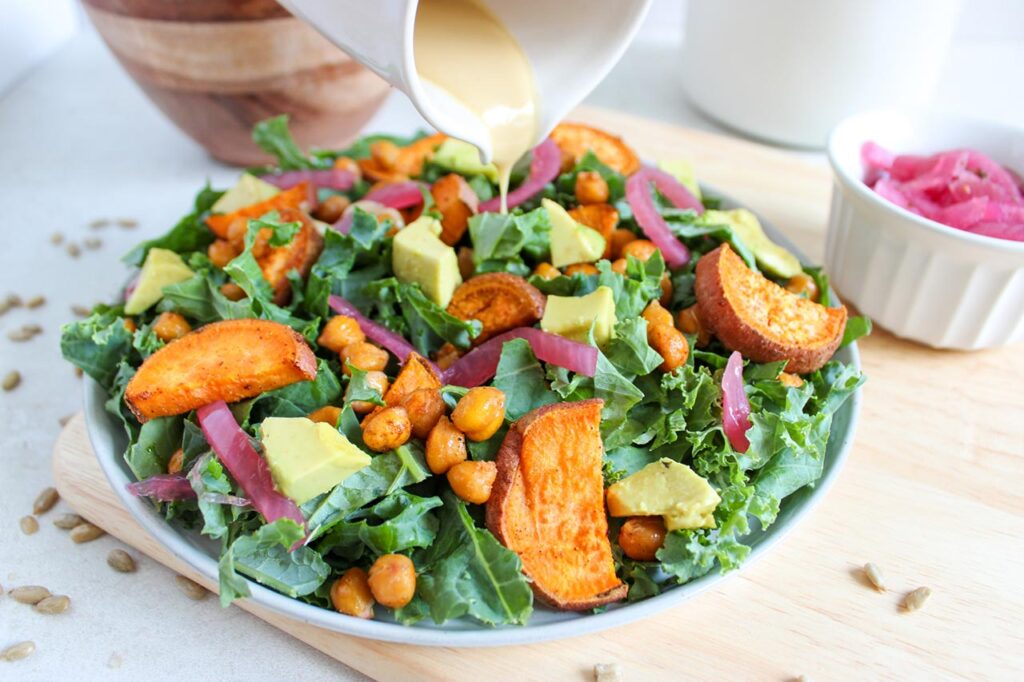 Dressing being poured over a fall harvest salad in na white bowl.