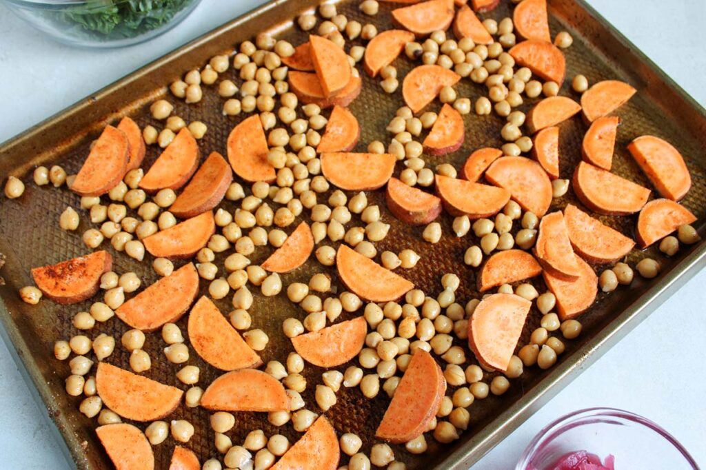 Cut sweet potatoes and chickpeas on a roasting pan.