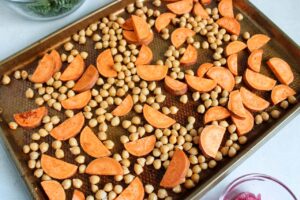 Cut sweet potatoes and chickpeas on a roasting pan.