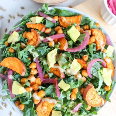 A fall harvest salad in a white bowl with tahini dressing drizzled over the top of the salad.