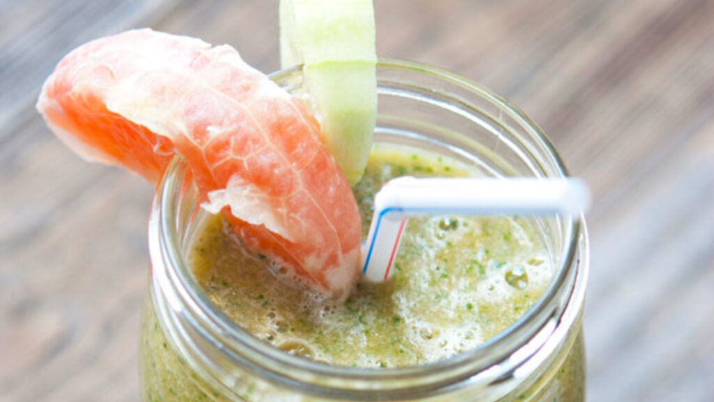 A mason jar filled with Grapefruit Smoothie has a wedge of grapefruit and cucumber on the edge of the jar for garnish.