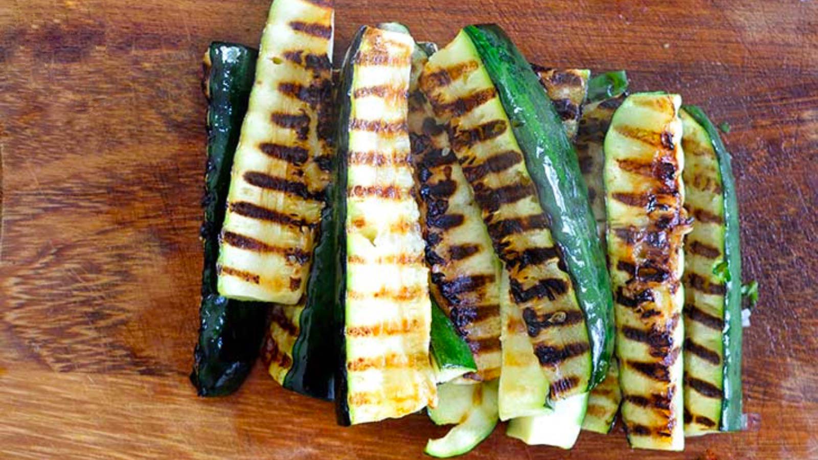 Grilled zucchini pieces laying on a wood cutting board
