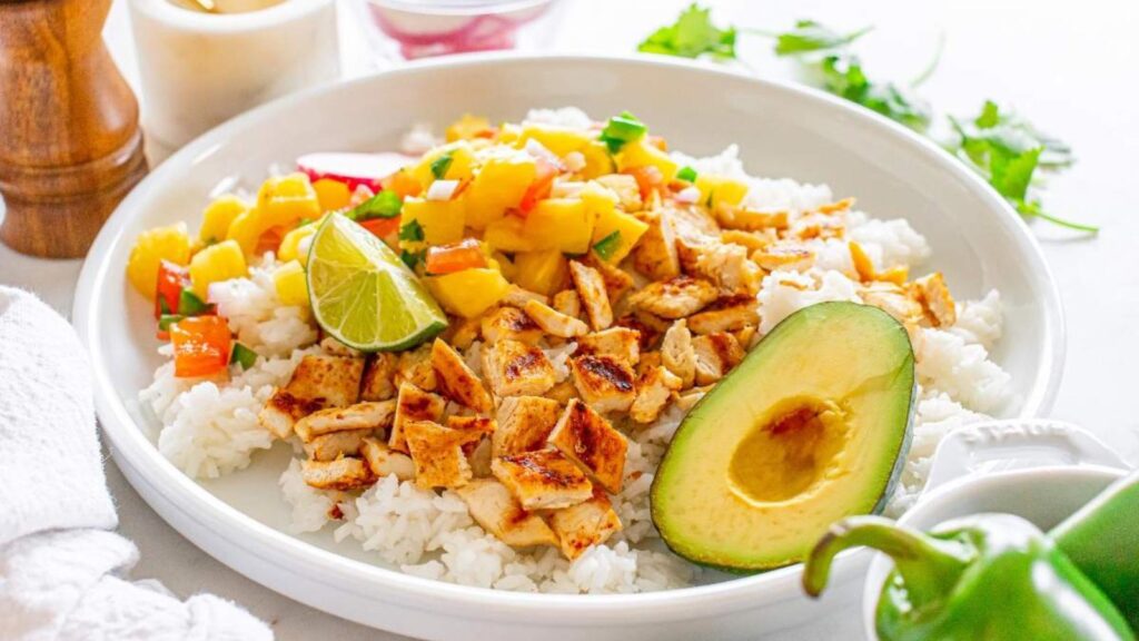 A white plates holds cut grilled chicken with pineapple salsa on a bed of rice.