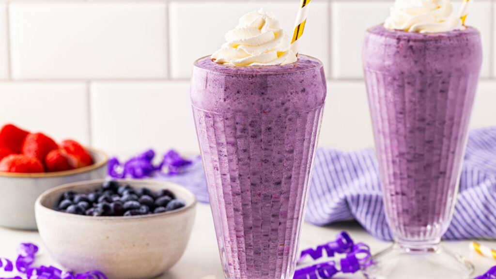 Two tall glasses filled with Grimace Shake and topped with whipped cream.