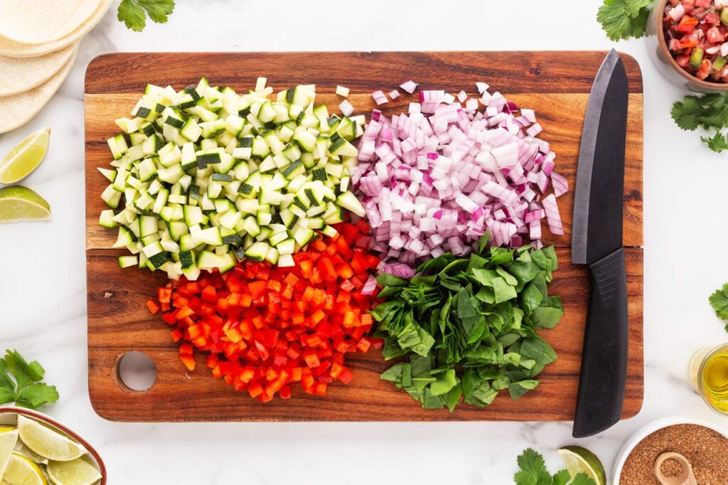 Chopped vegetables on a wood cutting board with a knife.