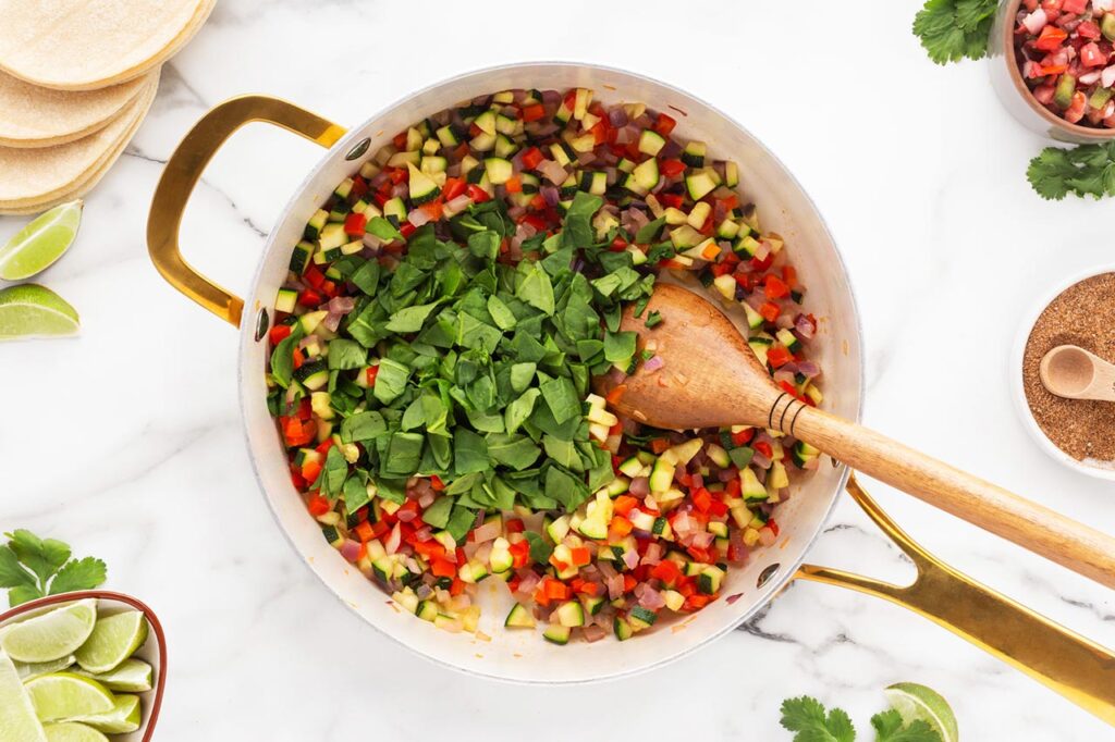Adding spinach to sautéing vegetables in a skillet.