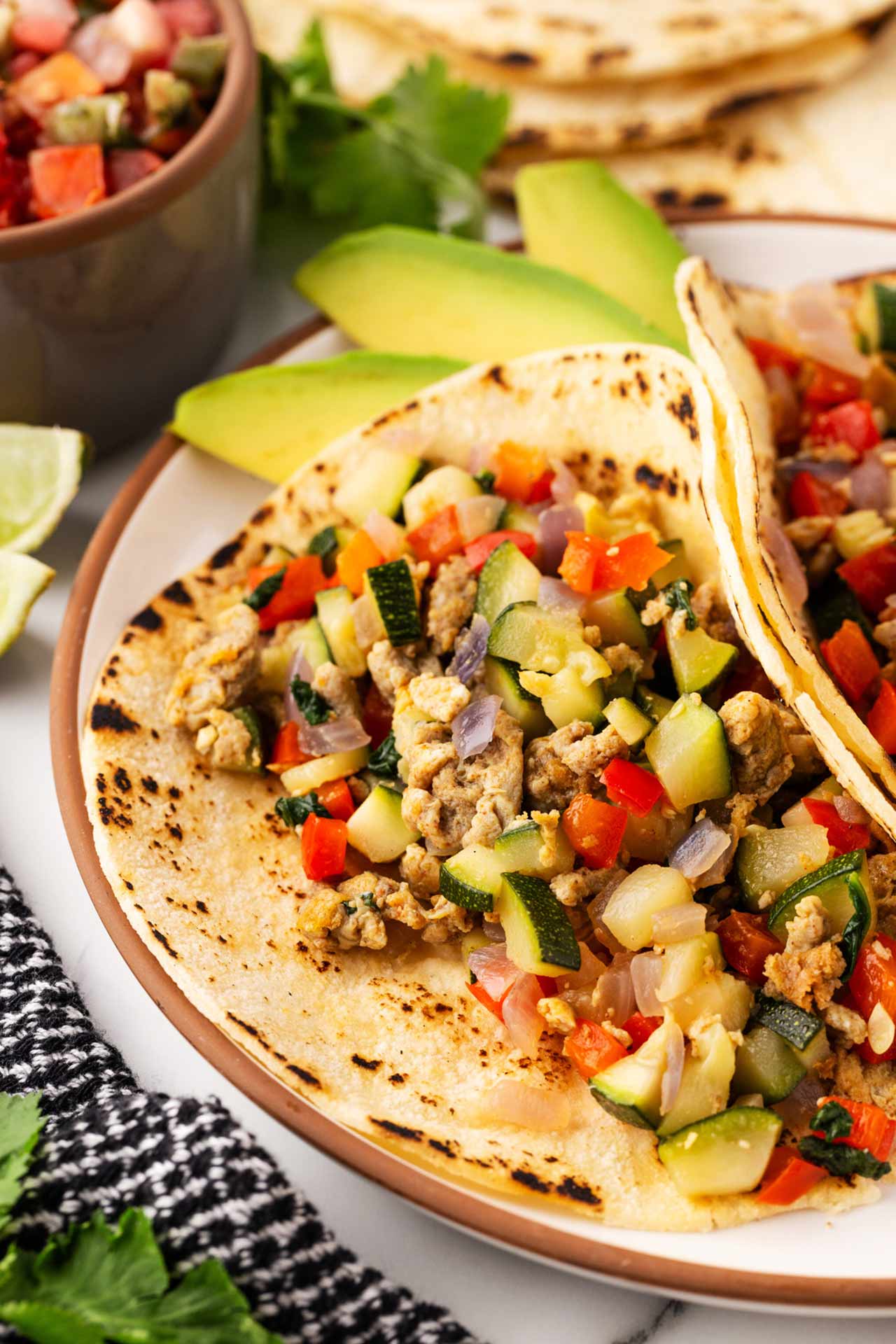 Two healthy breakfast tacos on a plate with avocado slices.