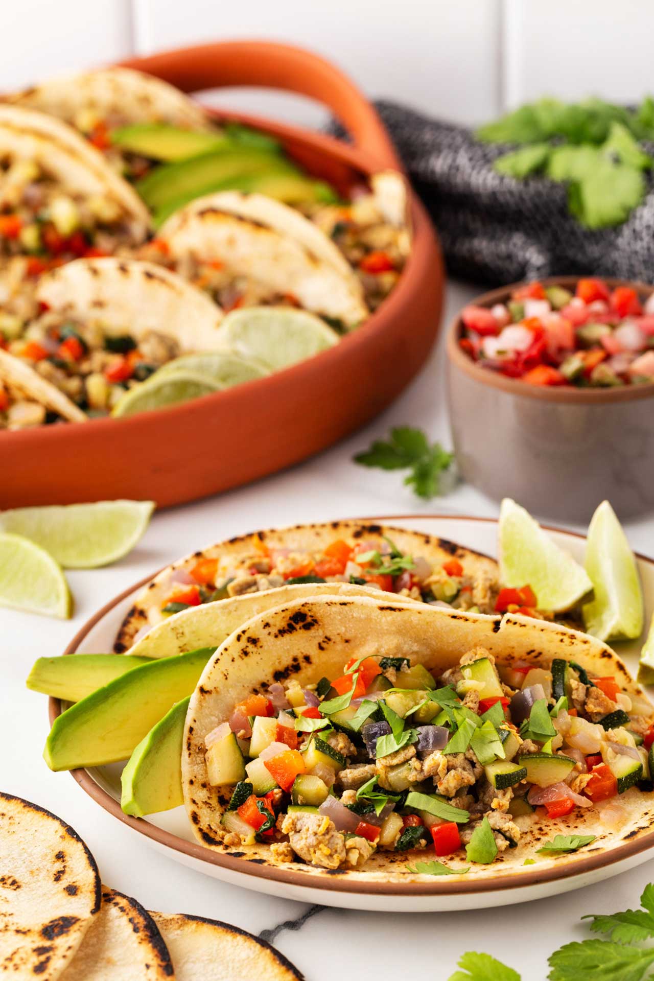 Two healthy breakfast tacos served on a white plate with avocado slices and lime wedges.