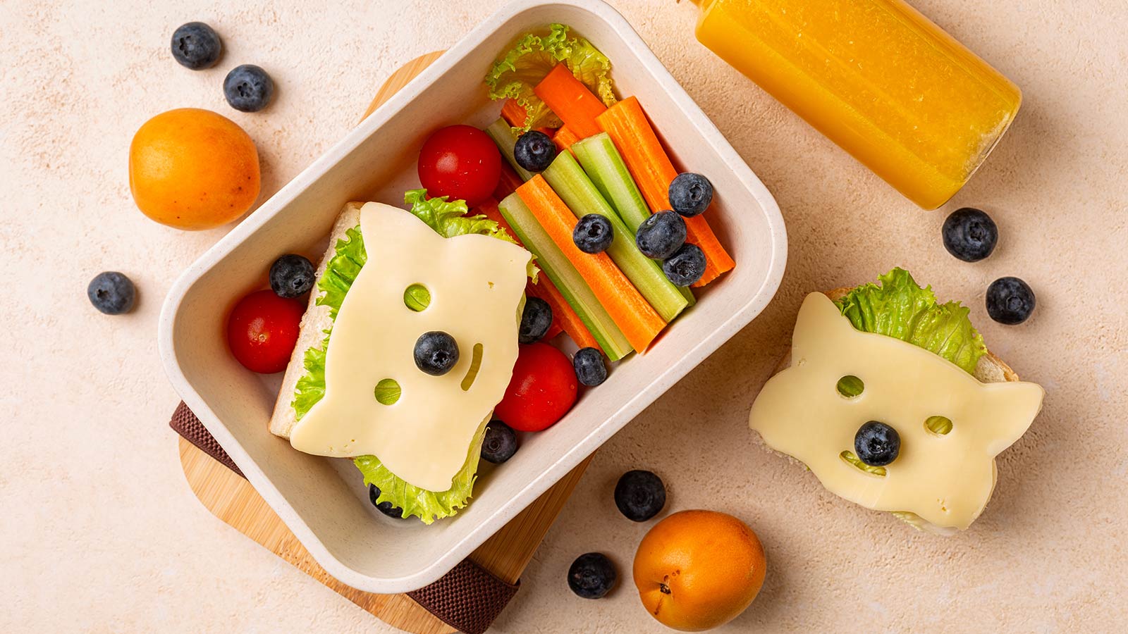 Kids school lunch box with funny fox sandwich with cheese, and fresh vegetables, carrot, tomatoes, celery, blueberries and apricots, orange juice. Back to school background. Top view.