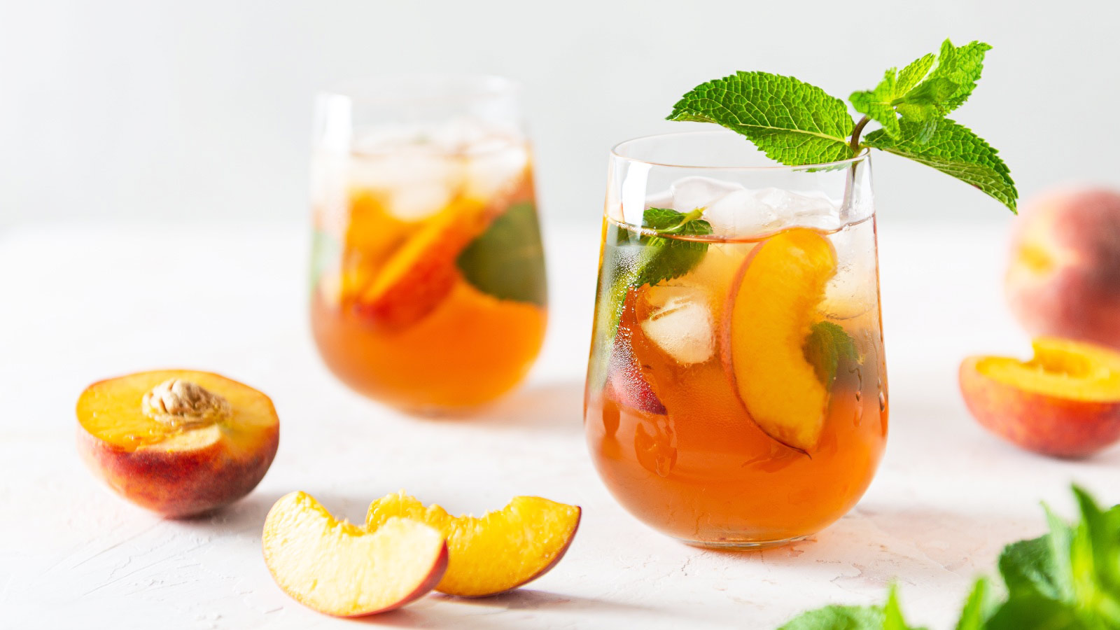 Fresh Peach iced tea. Iced tea with peach slices, mint and ice cubes on white background. Close up. Homemade refreshing summer drink recipe.