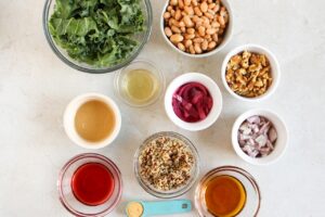 Kale Salad With Walnuts And Butter Beans Recipe ingredients in individual bowls on a white surface.