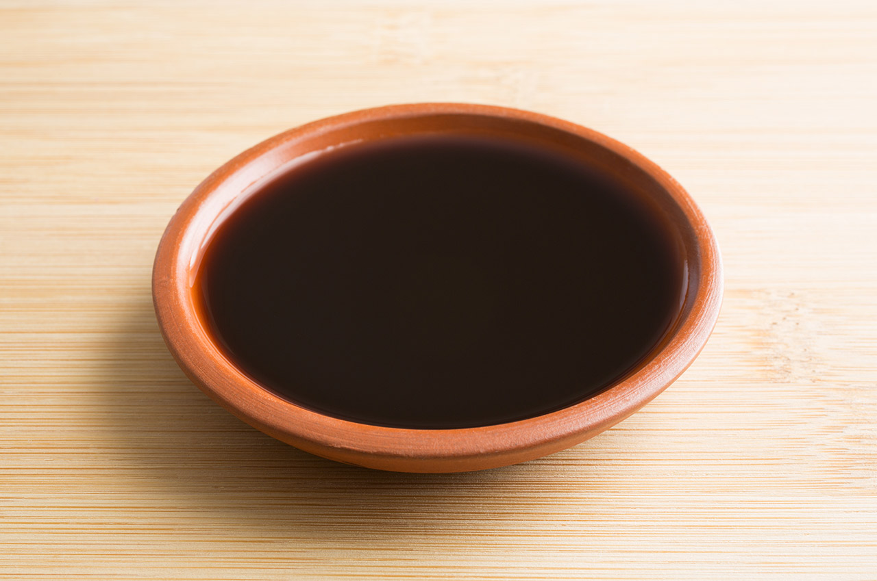 A small bowl filled with liquid smoke for cooking and barbecuing on a wood cutting board.