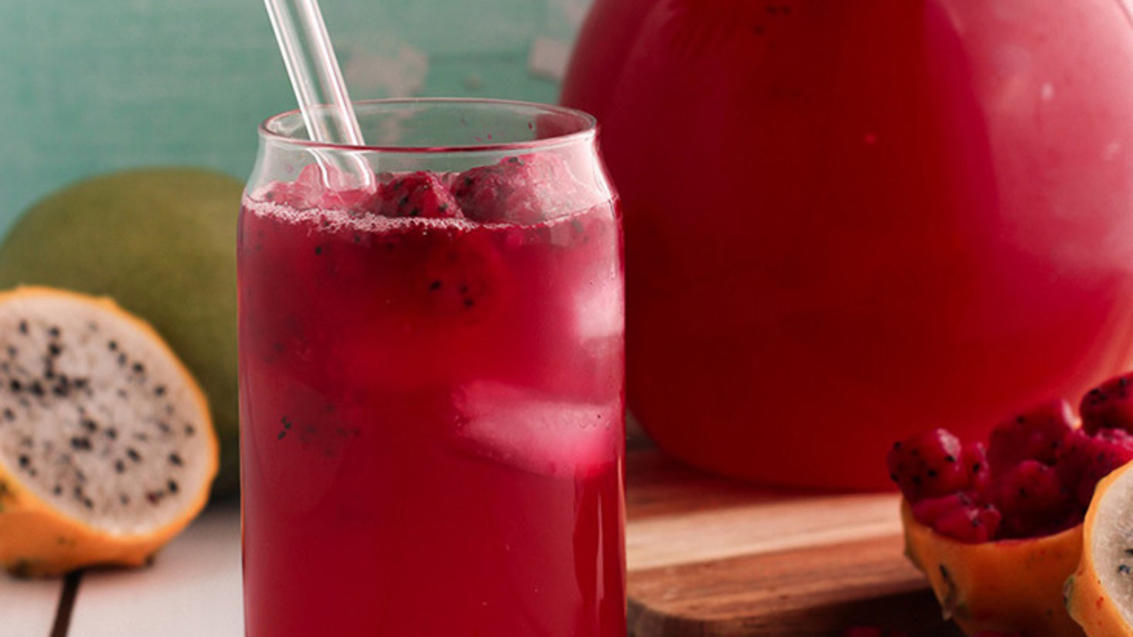 A glass of mango dragon fruit lemonade with a glass straw and chunks of dragon fruit in it.