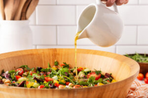 Pouring dressing over Mediterranean chopped salad in a wood salad bowl.