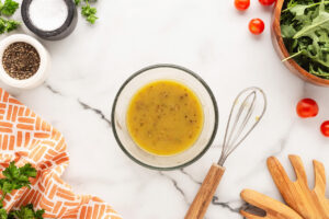 Whisked dressing in a glass bowl on a white surface.