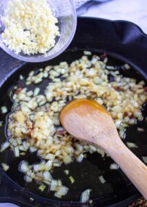 Adding garlic to onions in a skillet.