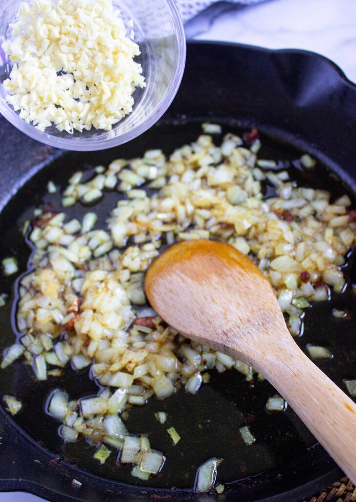 Adding garlic to onions in a skillet.