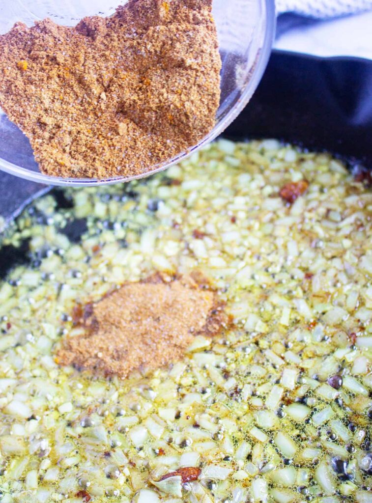 Adding spices to chopped onions in a skillet.