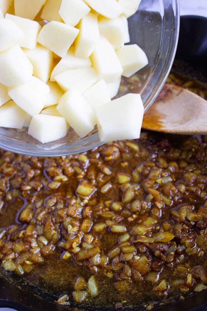 Adding cut potatoes to a skillet with onions.