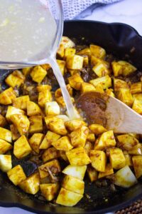 Pouring broth into a skillet with cut potatoes.