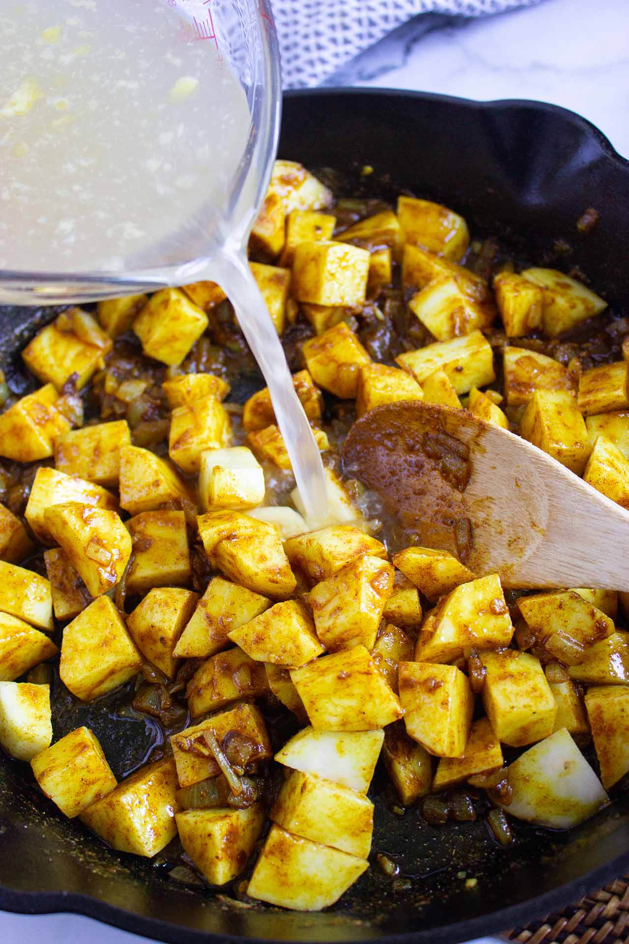 Pouring broth into a skillet with cut potatoes.