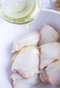 Pouring oil over chicken pieces in a bowl.