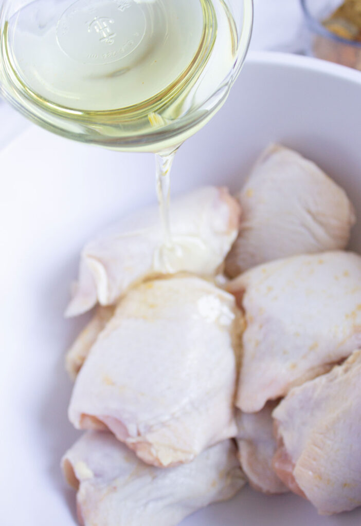 Pouring oil over chicken pieces in a bowl.