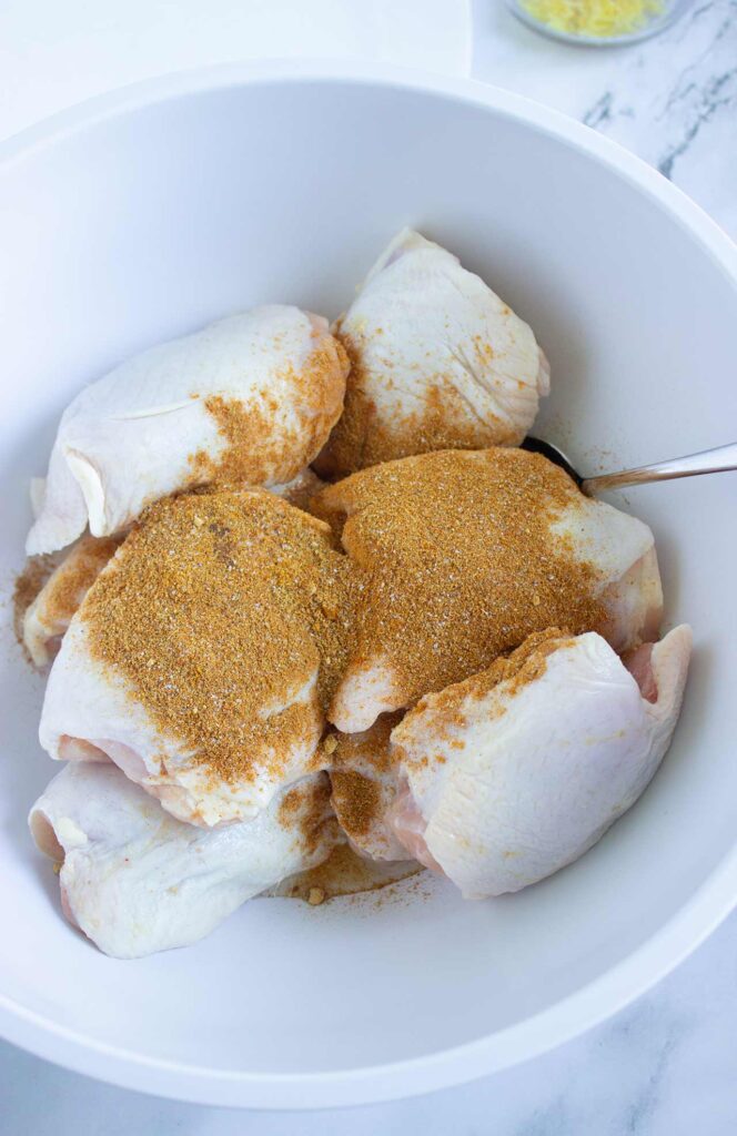 Spices added to chicken pieces in a mixing bowl.