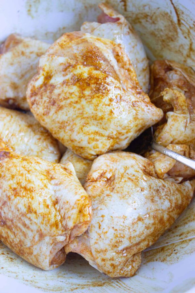 Chicken pieces tossed and coated in spices in a mixing bowl.