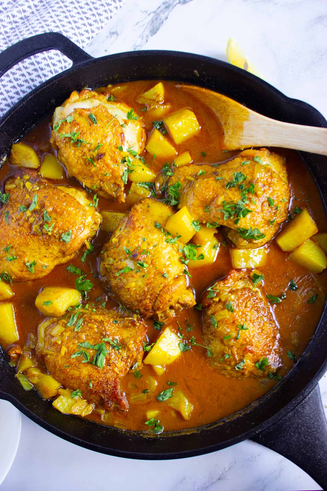 Overhead view of a cast iron skillet filled with chicken pieces, cut potatoes and sauce.