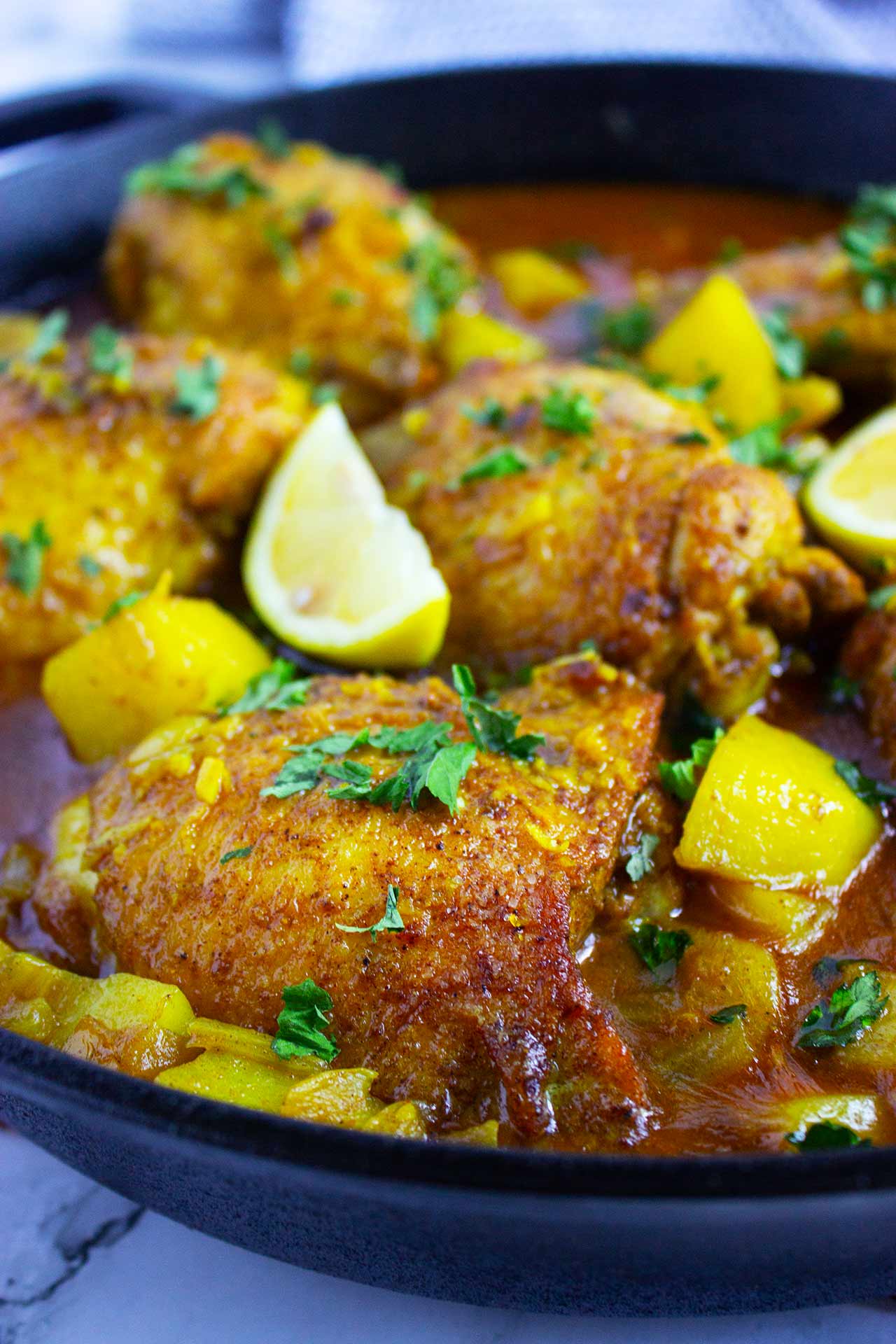 Side view of a black skillet filled with Moroccan chicken and cut potatoes in a delicious sauce.
