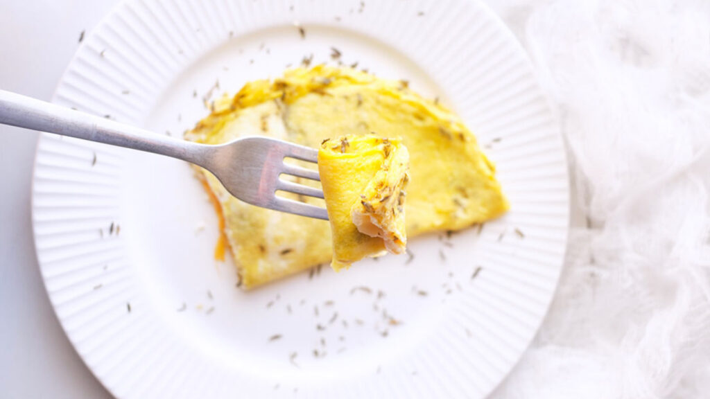 A fork lifts up a bite of a one egg omelet.