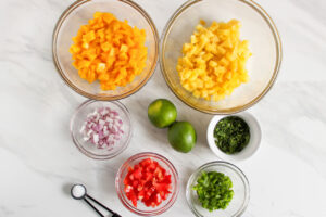 Ingredients for Pineapple Mango Salsa in individual bowls on a white surface.