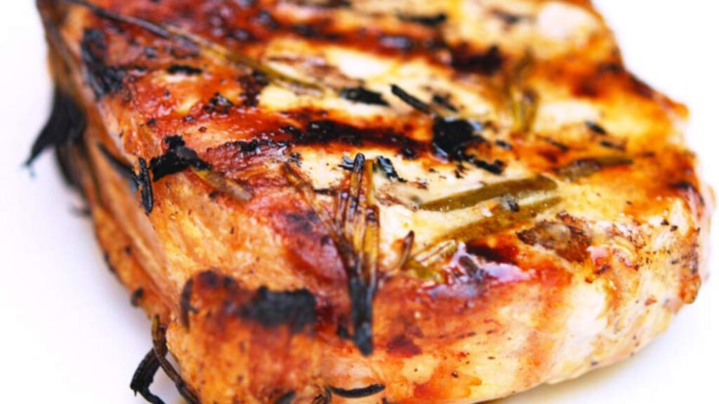 Closeup of a single rosemary pork chop on a white background.