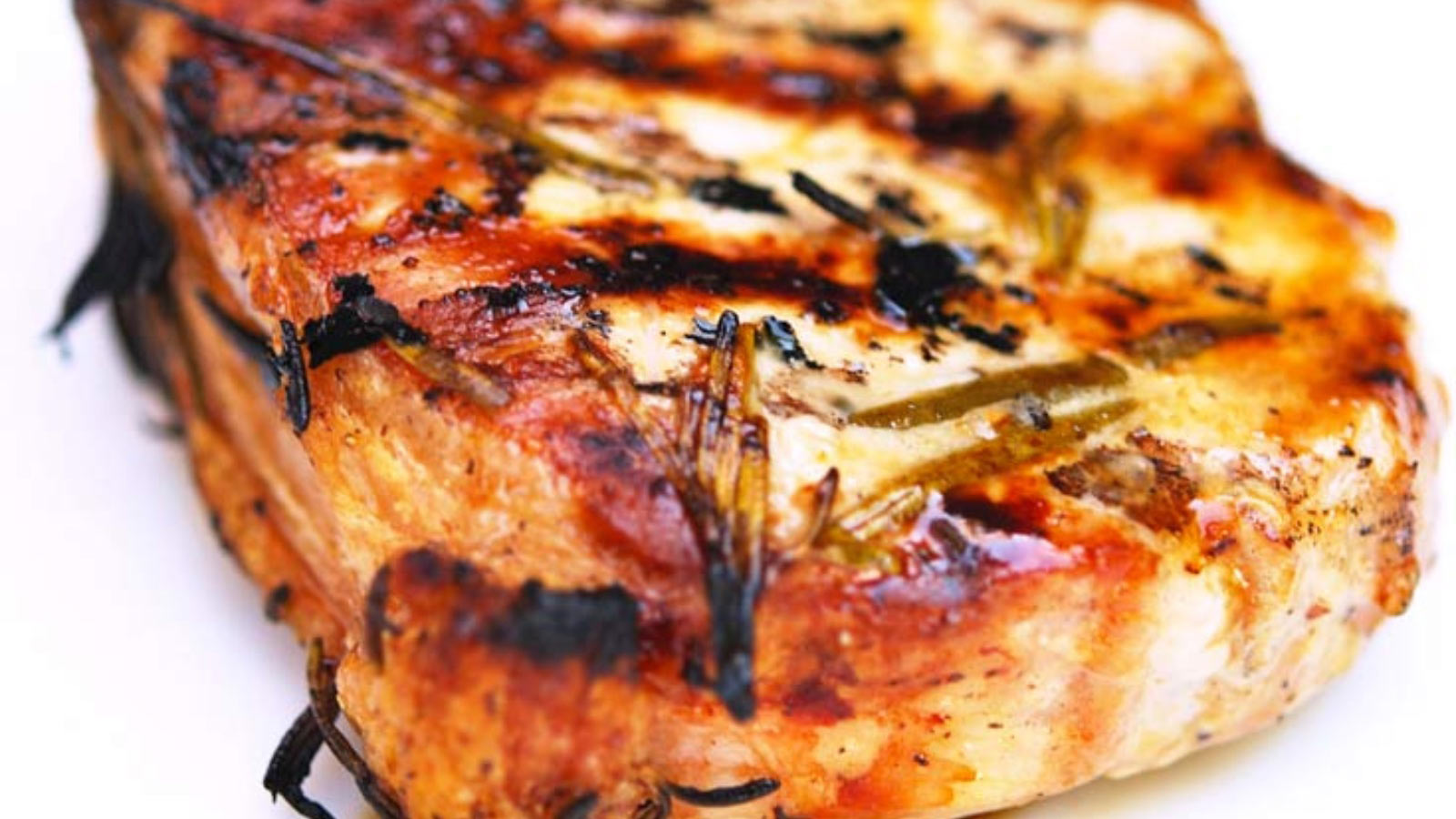 Closeup of a single rosemary pork chop on a white background.