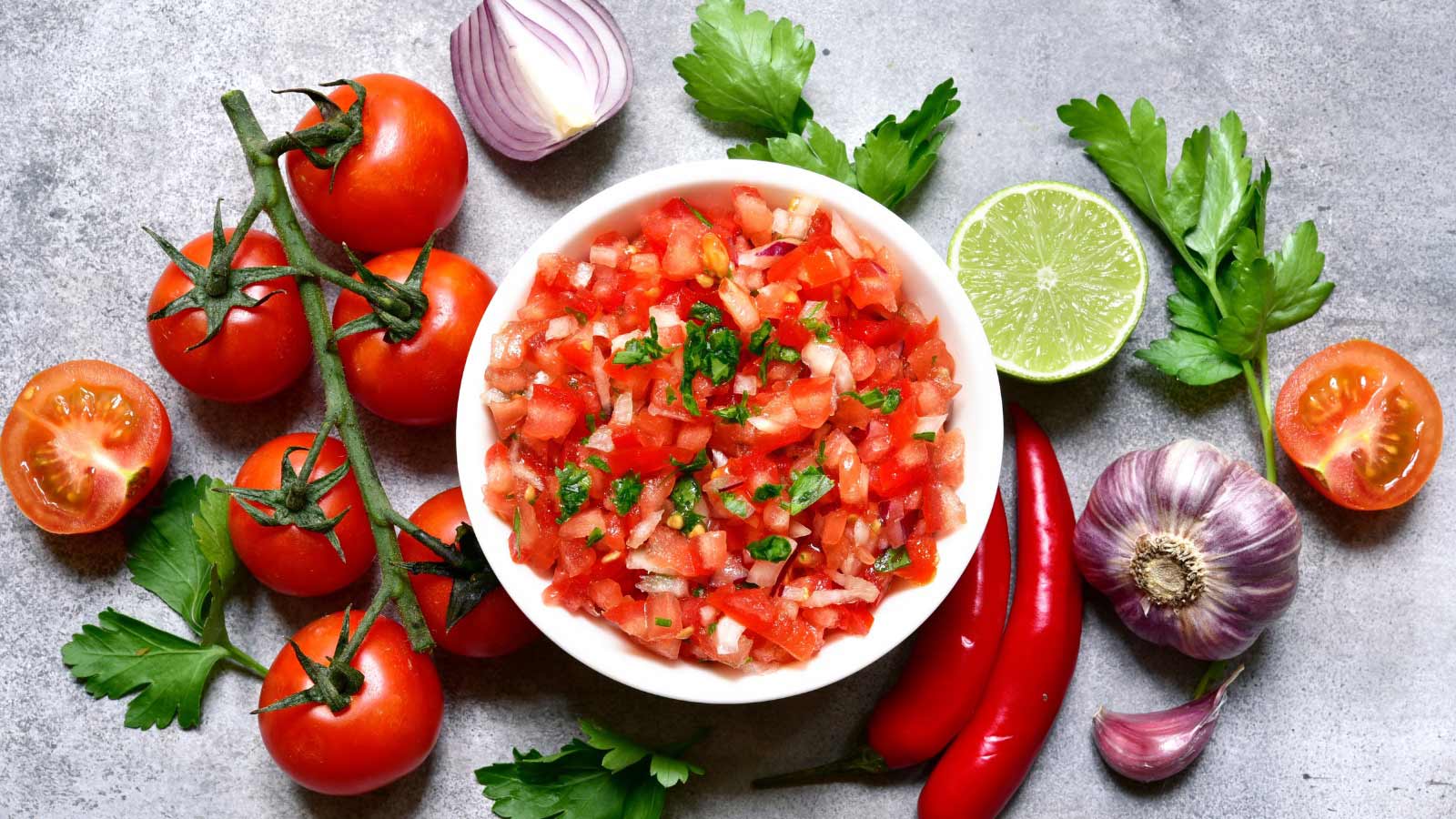 Tomato salsa - traditional mexican sauce with ingredients for making on a light grey slate,stone or concrete background.Top view with copy space.