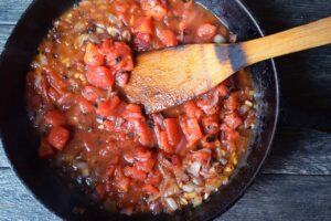 Diced tomatoes added to a skillet with onions and garlic.