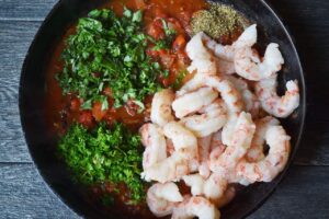 Shrimp and herbs added to a skillet with tomato sauce.