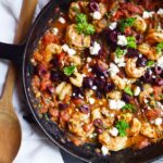 An overhead view of a skillet filled with Shrimp Saganaki and garnished with olives, feta, and fresh parsley.