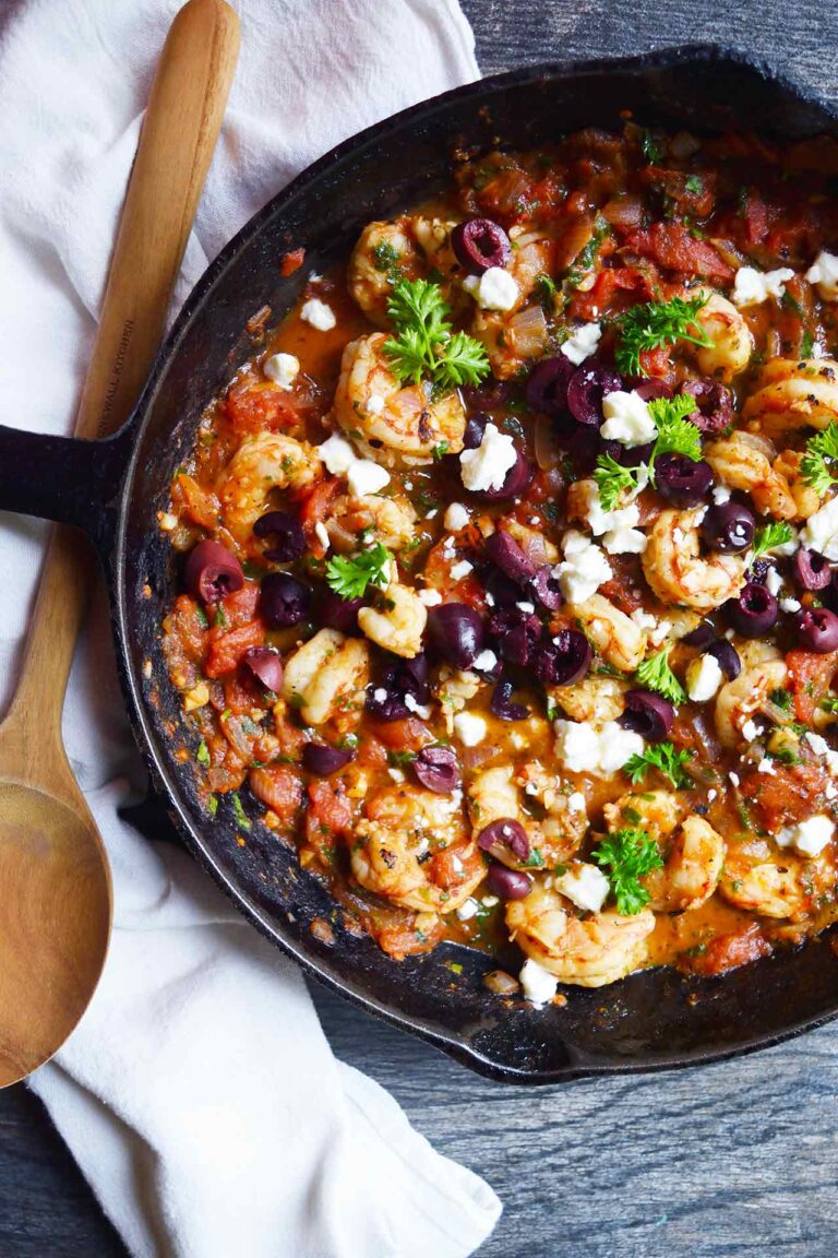 An overhead view of a skillet filled with Shrimp Saganaki and garnished with olives, feta, and fresh parsley.