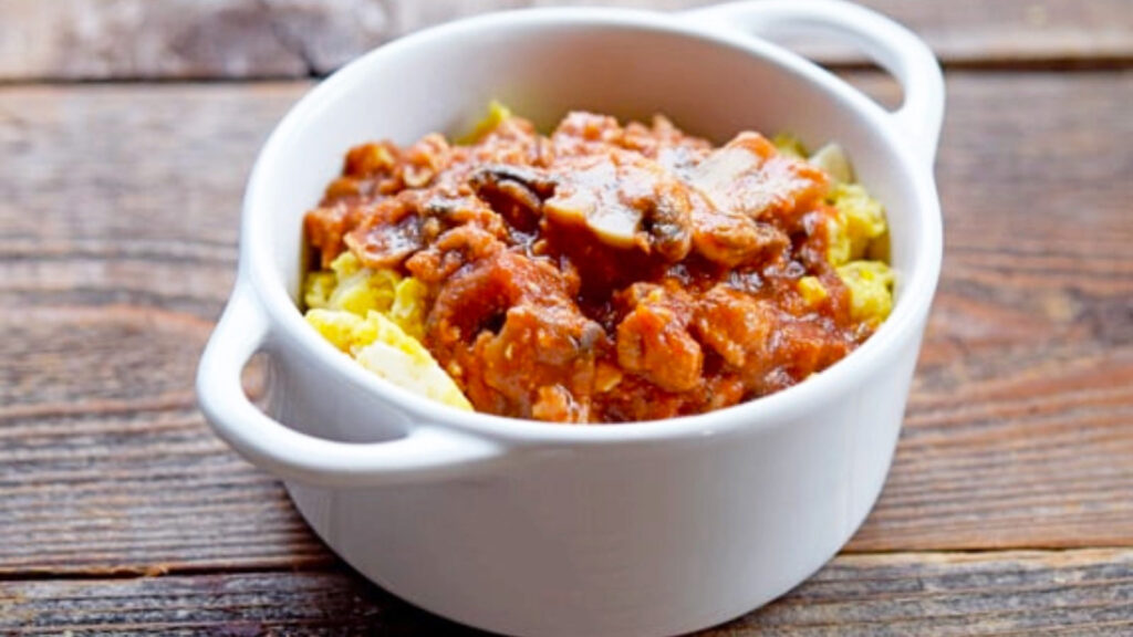 A small white crock is filled with scrambled eggs and topped off with spaghetti sauce.